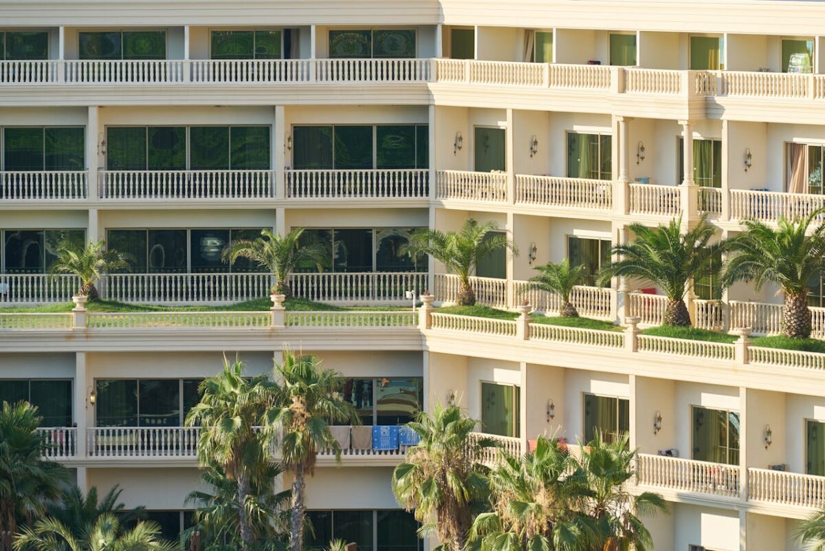 Elegant apartment building exterior with lush palm trees and balconies, ideal for vacation living.