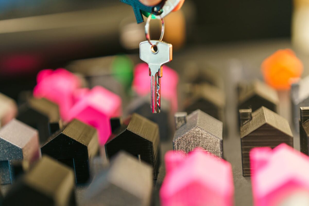 Close-up of a hand holding a key above colorful miniature houses, symbolizing real estate transaction or investment.