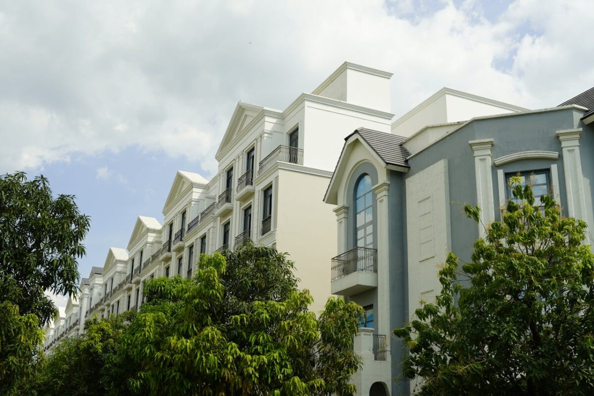 A modern residential building with classic architectural details surrounded by lush greenery under a partly cloudy sky.