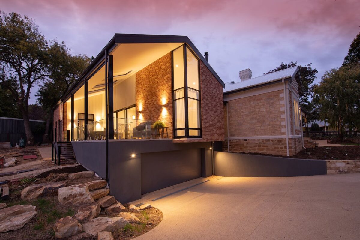 Modern dwelling house exterior with shiny lights near empty pathway under cloudy sky at sundown